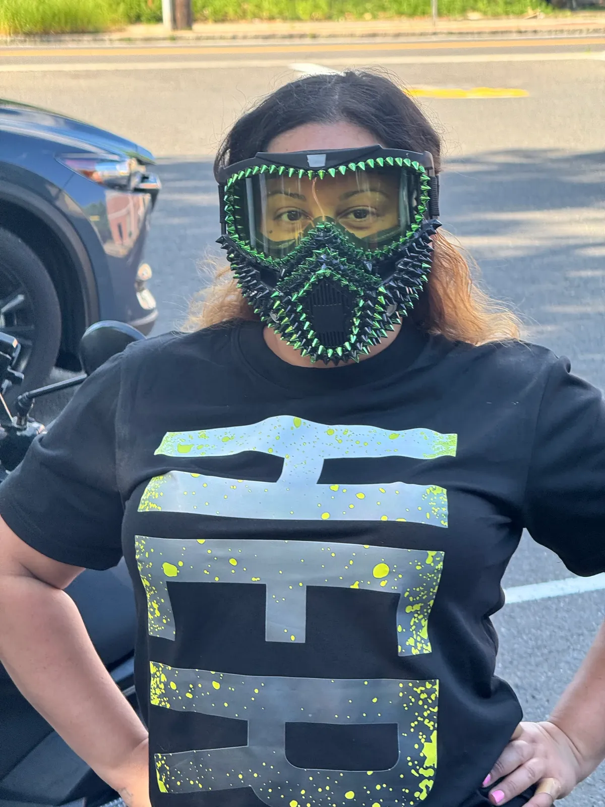 Rider wearing a green crystal face mask beside a car
