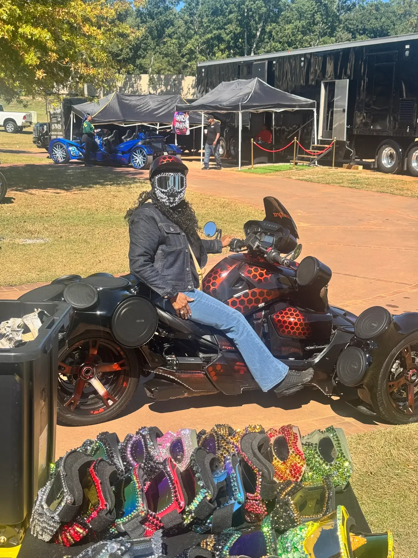 Rider wearing an embellished face covering on a three-wheel motorcycle at the festival