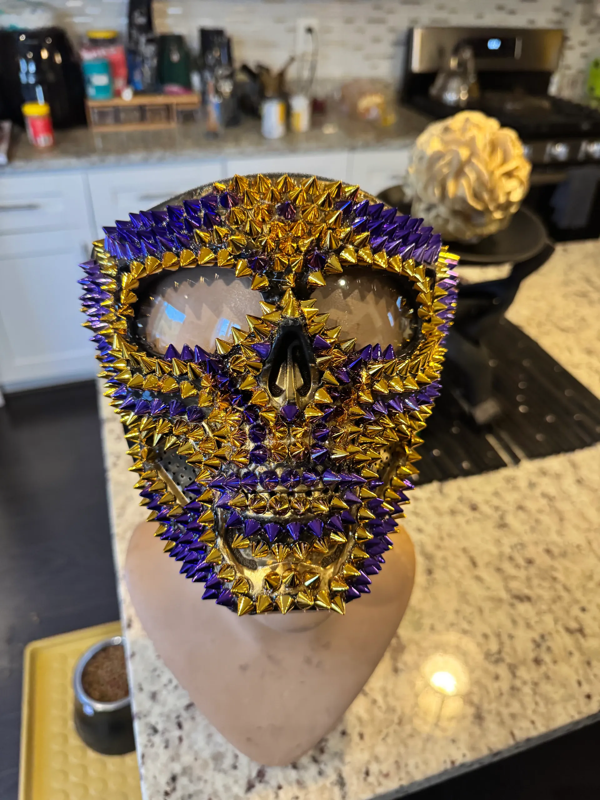 Close-up detail of the purple and gold spiked mask showing its metallic cone studs and crystal accents