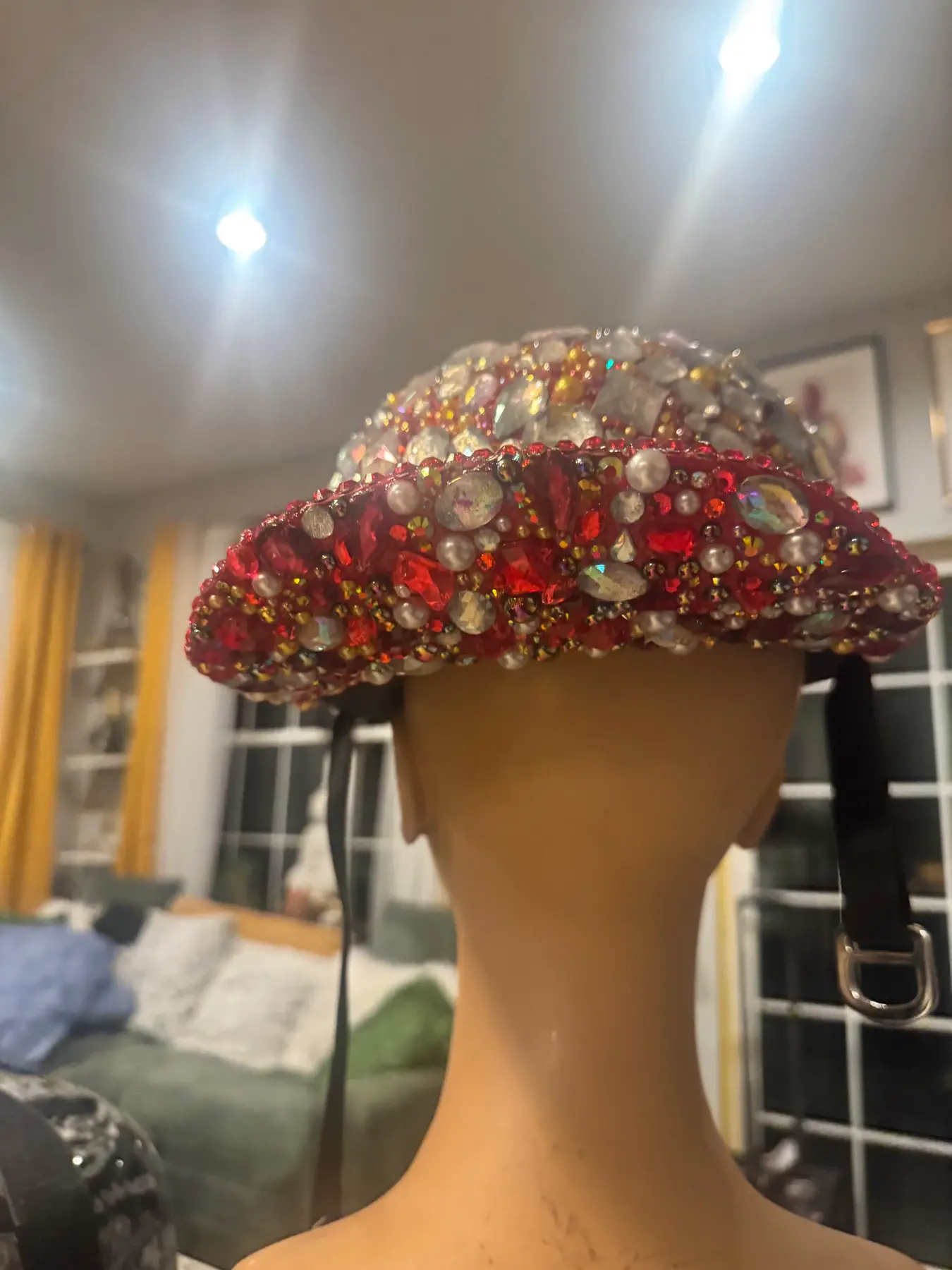 Side profile of a red ball cap helmet covered in crystals, pearls, and gold accents