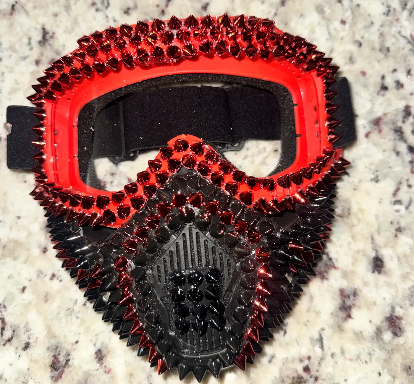 Flat-lay view of the red and black spiked mask with its clear lens visor and crystal spikes