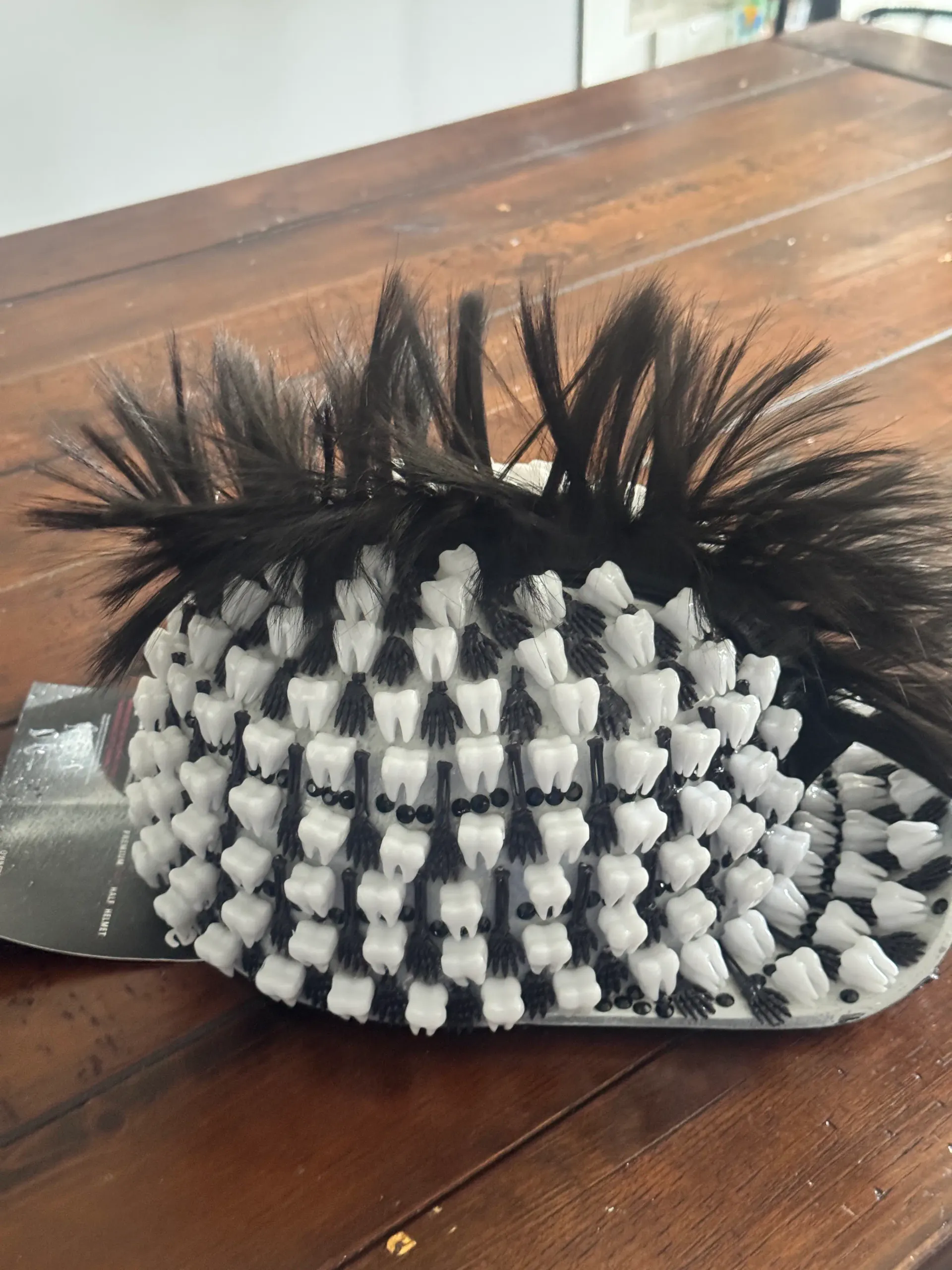 Overhead detail of the black teeth helmet shell with layered white teeth and rows of black beads on a wood table