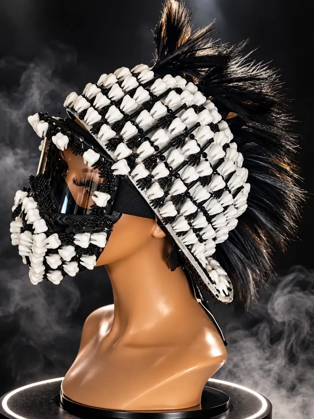 Three-quarter side view of the black teeth helmet with a clear visor, beaded trim, and feather mohawk on a mannequin bust